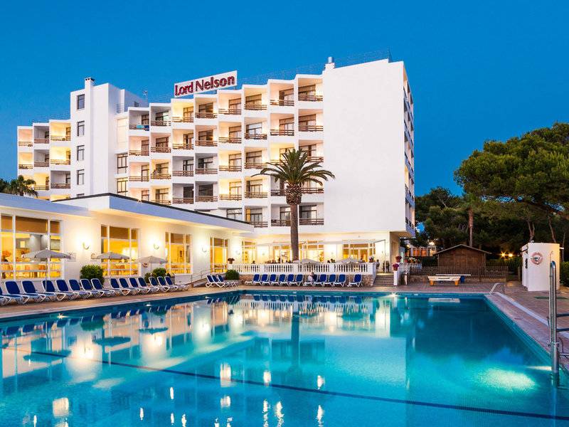 Außenansicht des Lord Nelson Hotels mit Pool bei Nachtbeleuchtung.