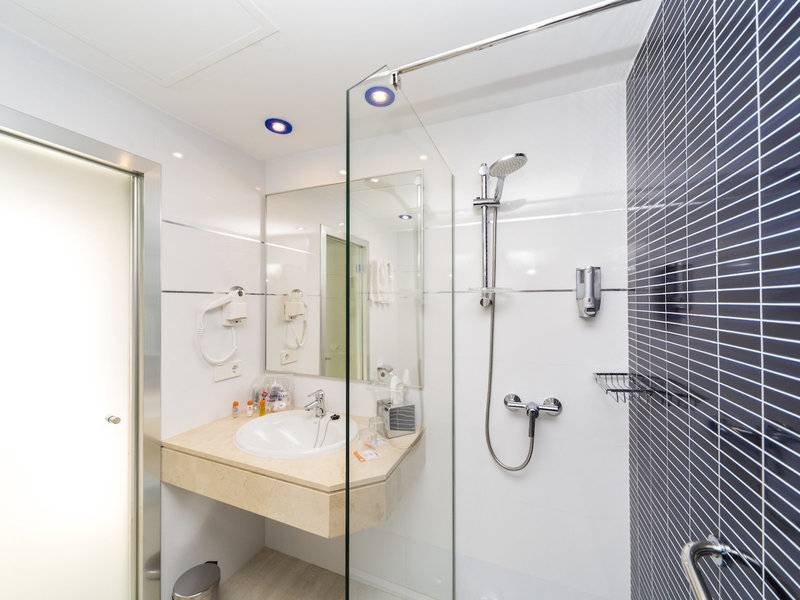 Badezimmer des Globales Lord Nelson Hotels mit Glasdusche, Waschbecken und Spiegel.