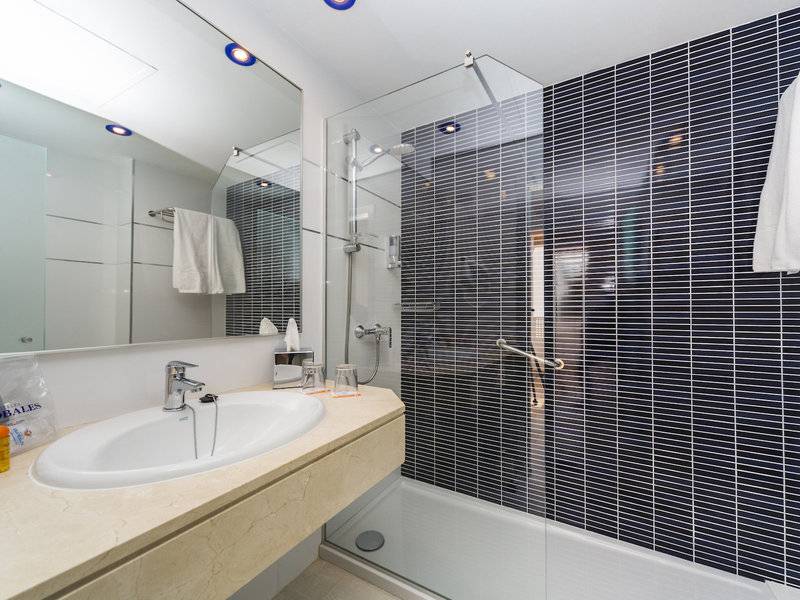 Ein Badezimmer im Hotel Globales Lord Nelson mit einer Dusche, einem Waschbecken und Spiegel.
