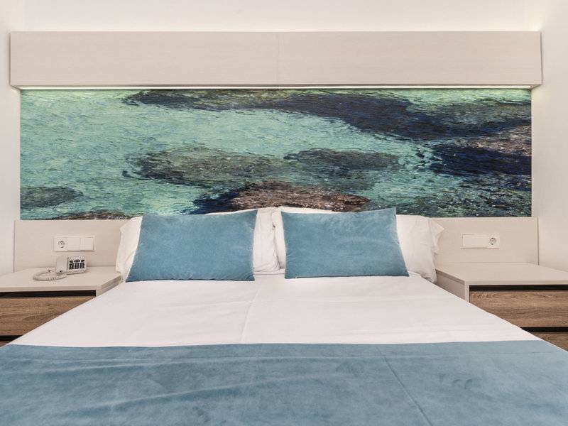 Schlafzimmer im Globales Lord Nelson Hotel mit blauem Ozeanbild und bequemem Bett.