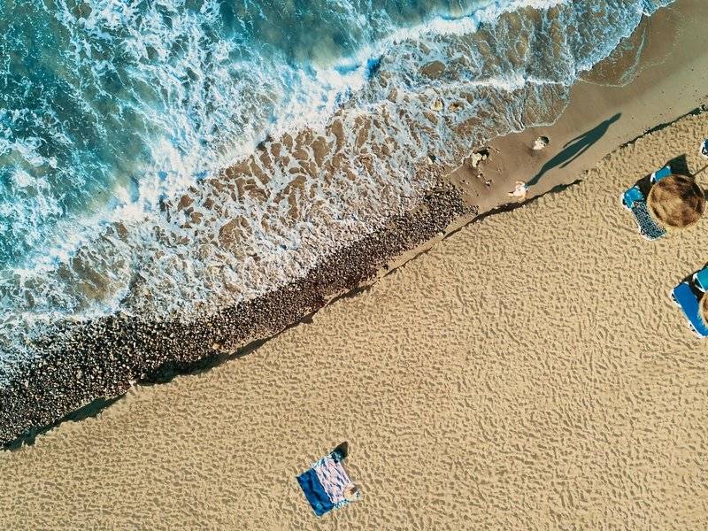 Oberflächenaufnahme von einem Strand mit Wellen und Sonne, mit Liegen und Handtüchern.