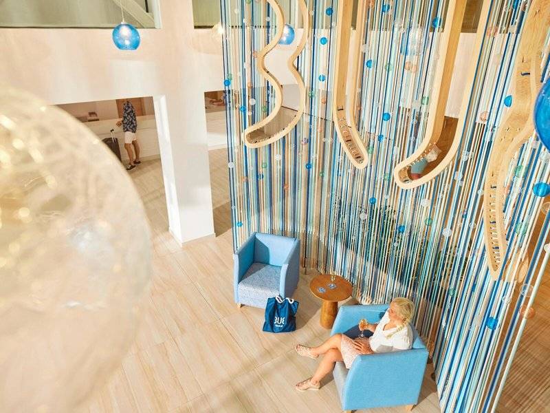 Ein Blick in die Lounge des Victoria Menorca Hotels mit einer Frau auf einem blauen Stuhl.