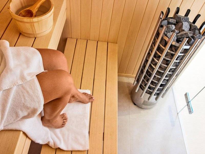 Person in einer Holzsauna im Victoria Menorca Hotel mit einem Holzeimer und einem vollen Kohlebecken.