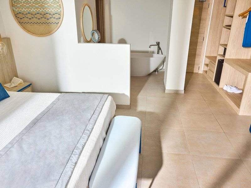 Innenansicht des Schlafzimmers im Victoria Menorca Hotel mit Bett, Badewanne und Kleiderschrank.