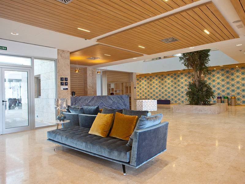 Lobby des Seth 55 Santo Tomás Hotels mit grauem Sofa, gelben Kissen und zentralem Baum.