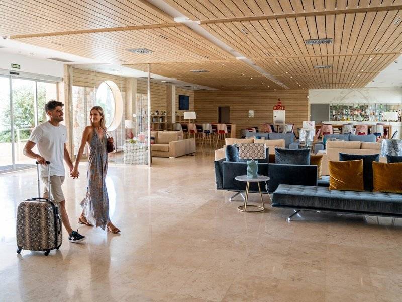 Ein Paar im Eingangsbereich des Seth 55 Santo Tomás Hotels, beide tragen Lächeln, während sie sich mit Gepäck durch die geräumige Lobby bewegen.