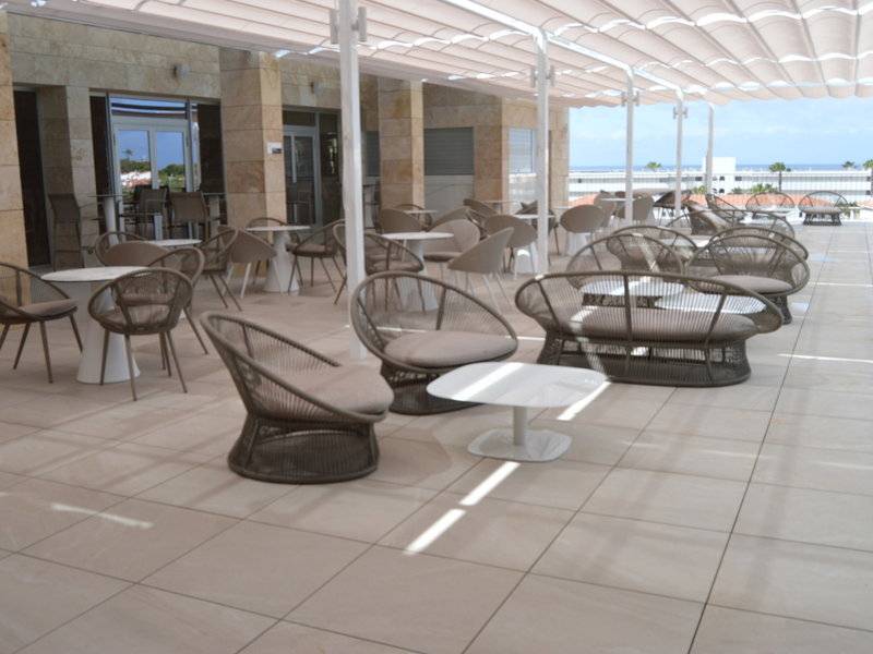 Hotelterrasse mit Tischen und Stühlen unter einem Sonnendach im Freien.