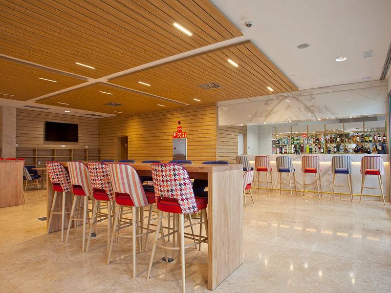 Innenbereich der Bar im Seth 55 Santo Tomás Hotel mit Holztischen, farbenfrohen Stühlen und einer Bar im Hintergrund.