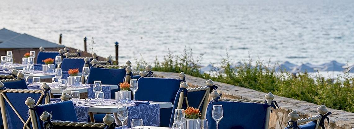 Blick auf das Restaurant des Aldemar Olympian Village mit Tischen und Stühlen am Meer.