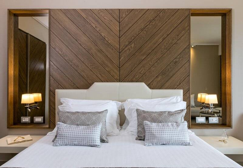 Schlafzimmer im Miraggio Thermal Spa Resort mit Bett, Kissen, Lampen und Holzwand.
