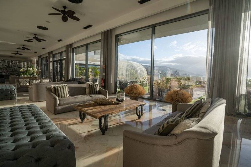 Lobby des Baia Azul Hotels mit Sofas, Tischen und großer Aussicht auf die Stadt.