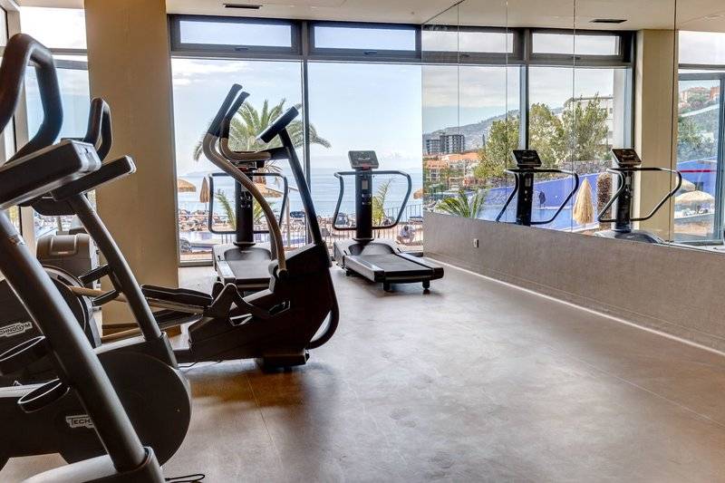 Fitnessbereich im Baia Azul Hotel mit Blick auf das Meer und eine Stadt.