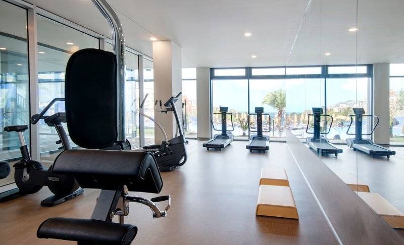Fitnessbereich des Baia Azul Hotels mit modernen Geräten und großen Fenstern.