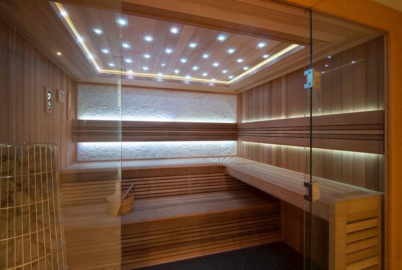 Innenansicht der Sauna im Baia Azul Hotel mit Holzwänden und Bänken, beleuchteter Decke und Glastür.