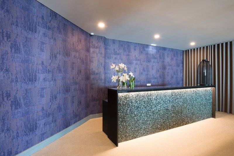 Empfangsbereich des Baia Azul Hotels mit blauen Wandverkleidungen und einer Theke mit Blumenarrangement.