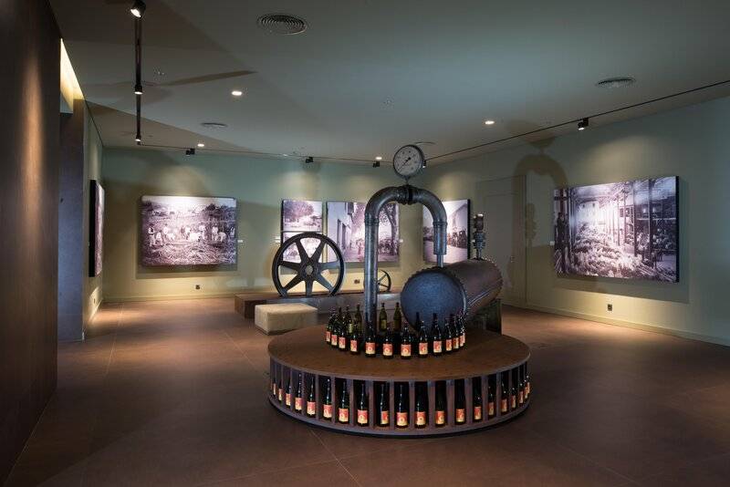 Ausstellungsraum im Saccharum Hotel mit Flaschen auf einem Industrie-Design und alten Fotografien an der Wand.