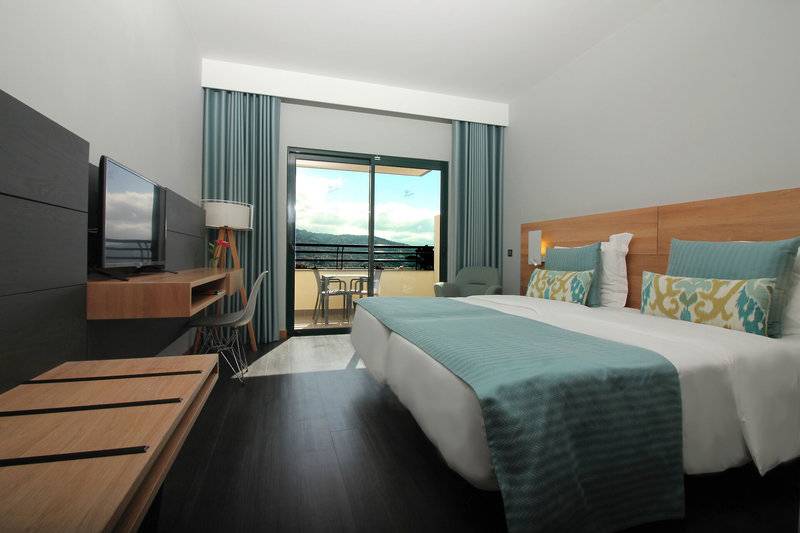 Doppelzimmer mit Balkon im Madeira Panorâmico Hotel, mit bequemen Betten, Fernseher und einem Schreibtisch.