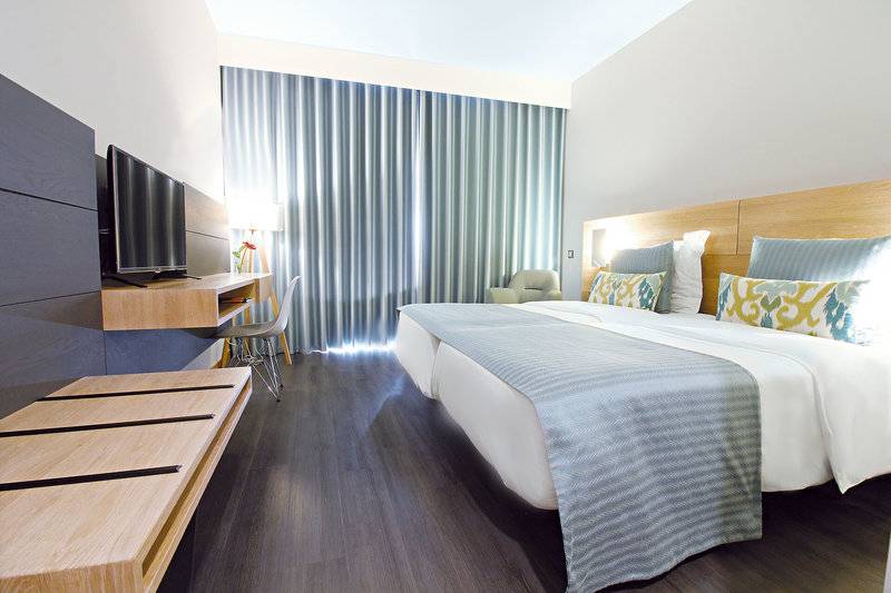 Doppelzimmer im Madeira Panorâmico Hotel mit zwei Betten, Fernseher, Schreibtisch und Vorhängen.