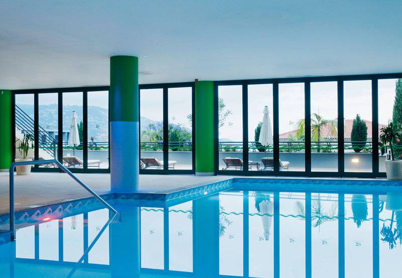 Innenansicht des Schwimmbads im Madeira Panoramic Hotel mit blauem Wasser und großen Fenstern.