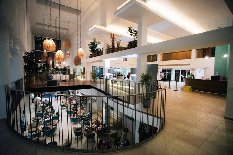Innenansicht der Lobby des Views Oasis Hotel mit mehreren Gästen, Tischen, Stühlen und Pflanzen.
