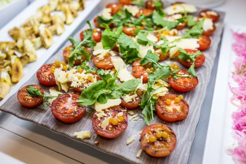 Gegrillte Tomaten mit Käse und Rucola auf einem Holzbrett serviert