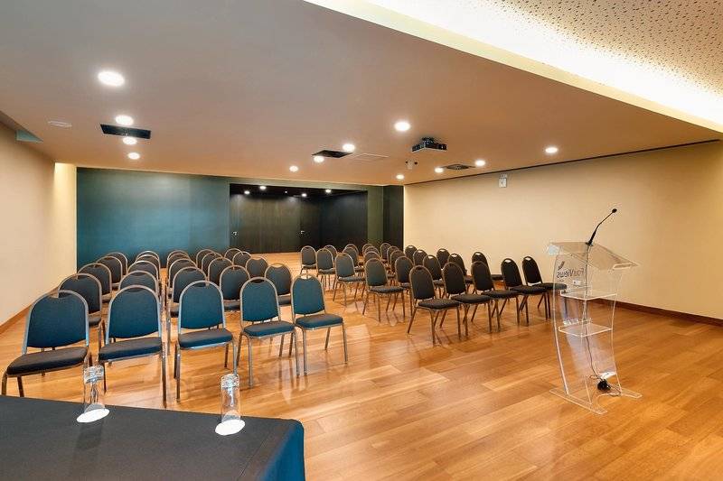 Konferenzraum im Views Baia Hotel mit blauen Stühlen, Glastischen und einem Rednerpult.