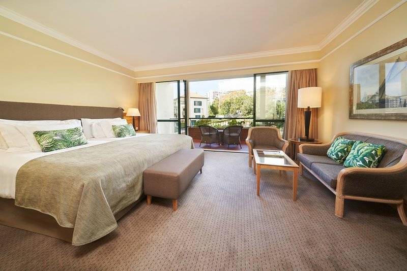 Hotelzimmer im Cliff Bay mit großem Bett, Wohnzimmerbereich und Balkon.