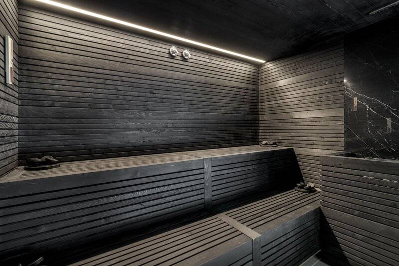 Innenansicht der Sauna im Royal Savoy Hotel mit schwarzen Holzwänden und Bänken.