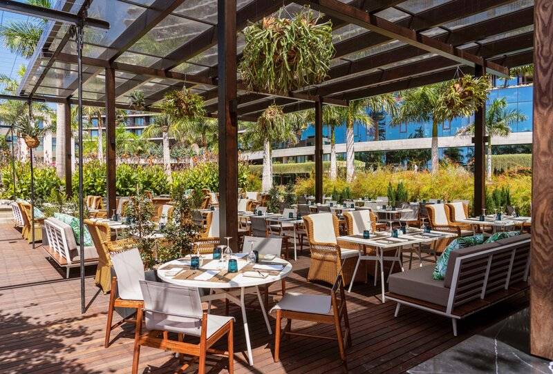 Außenbereich des Savoy Palace Gartenrestaurants mit Holzböden und hängenden Pflanzen.