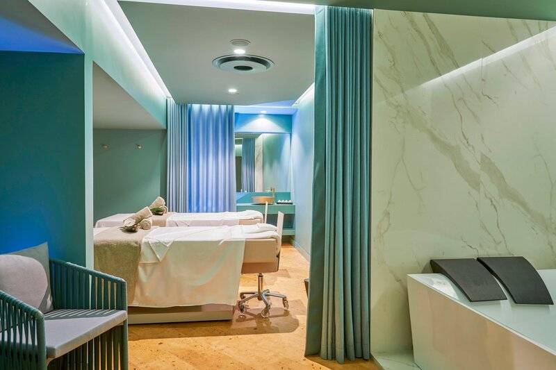 Spa-Behandlungsraum im Savoy Palace Hotel mit zwei Liegen, blauen Vorhängen und Marmorwand.