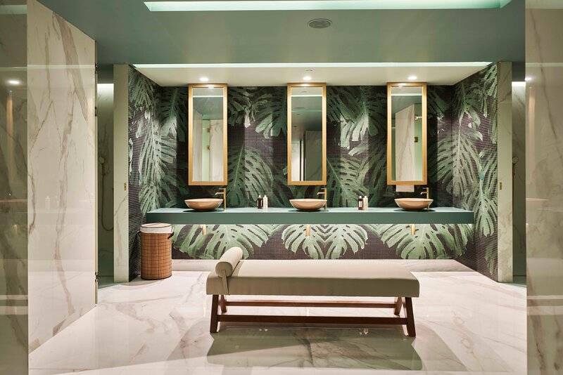 Badezimmer im Savoy Palace mit tropischen Tapeten, drei Waschbecken und Spiegeln, einer Bank und Marmorböden.