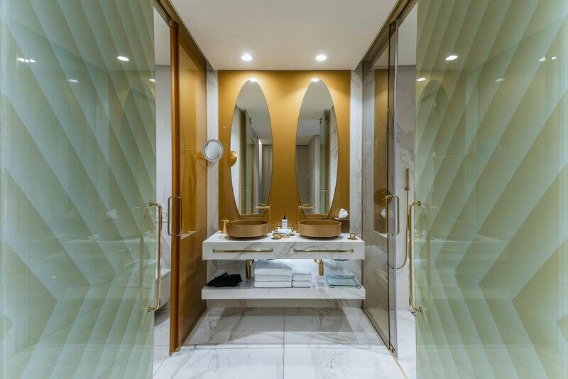 Das Badezimmer des Savoy Palace mit zwei Waschbecken, Spiegeln und gemusterten Glaswänden.