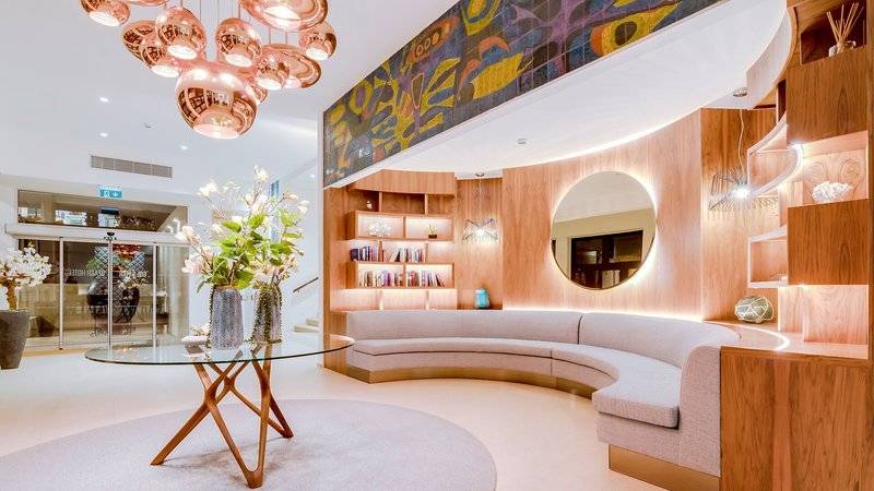 Lobby des Sol e Mar Hotels mit runden Tisch, Blumenvase, ovalem Spiegel und holzvertäfelten Wänden