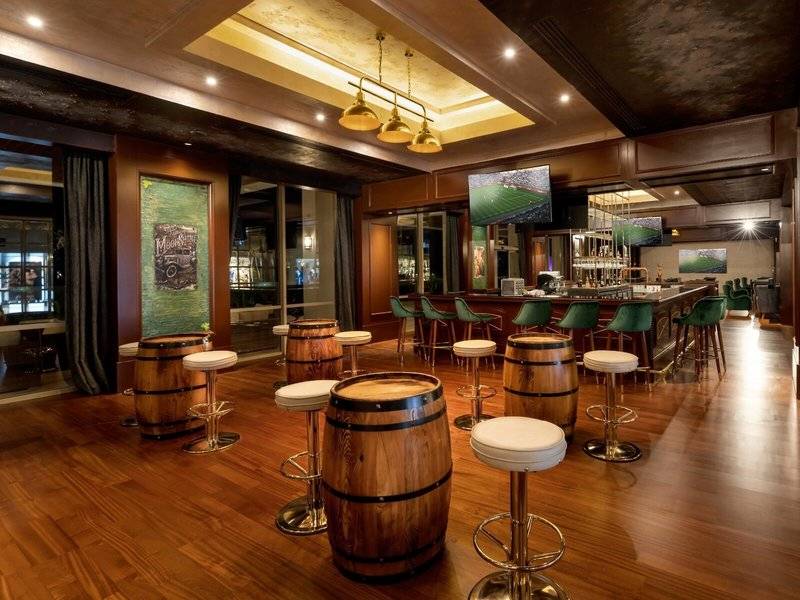 Innenansicht der Bar im Rixos Premium Belek Hotel mit hölzernem Boden und grünen Stühlen.