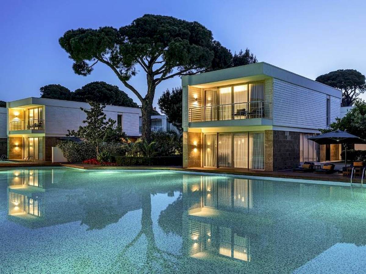 Poolansicht des Rixos Premium Belek Hotels mit zwei Gebäuden und Bäumen bei Nacht