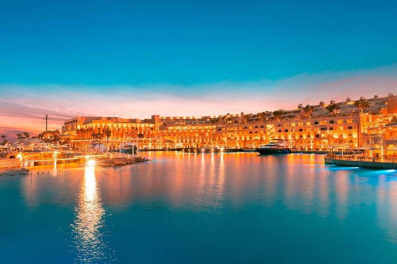 Pickalbatros Citadel Resort am Abend mit beleuchteten Gebäuden und Booten im Hafen.