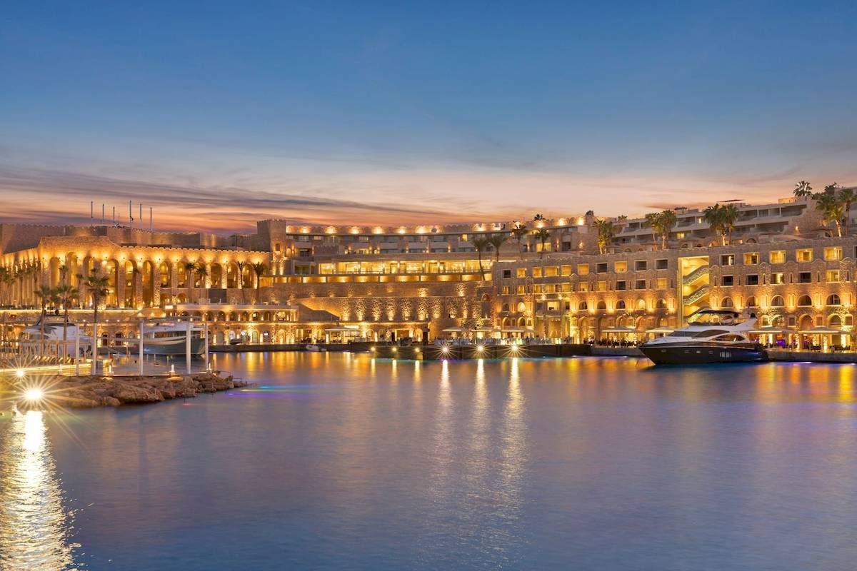 Pickalbatros Citadel Resort bei Sonnenuntergang mit beleuchteten Gebäuden und Yachten im Hafen.