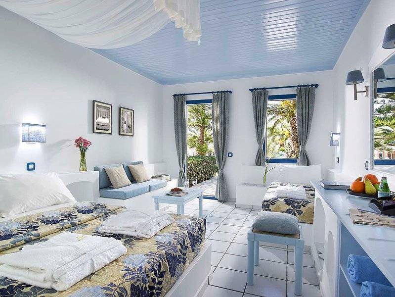 Schlafzimmer im Mitsis Cretan Village Hotel mit weißen Möbeln, blauer Decke und offenem Fenster.