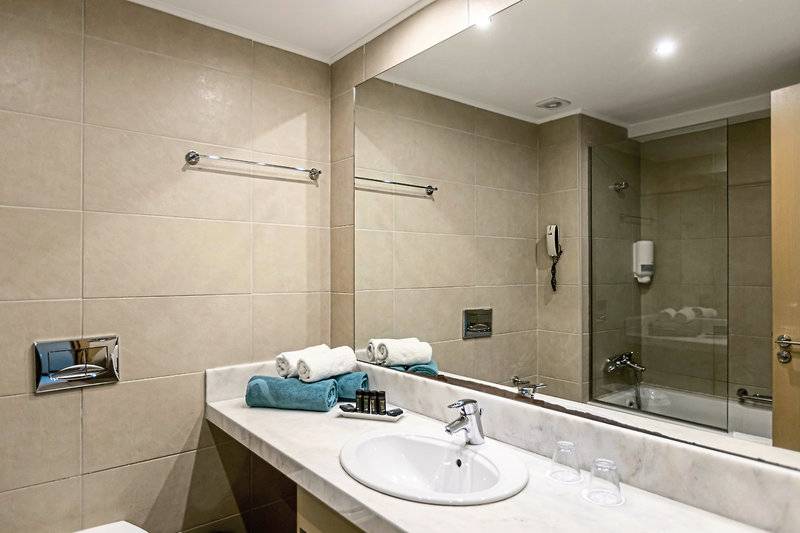 Badezimmer im Asterias Beach Resort mit Waschbecken, Spiegel und Duschbereich.