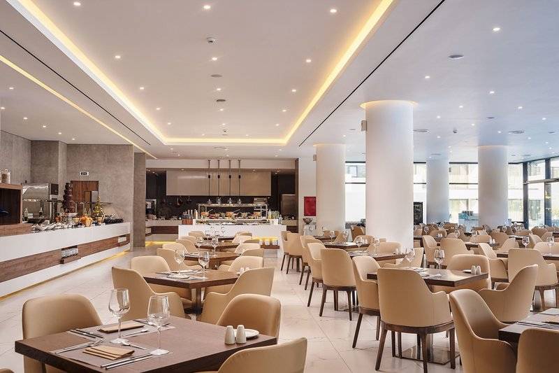 Innenansicht des Restaurants im Lindos Grand Resort & Spa mit leeren Tischen und Stühlen.