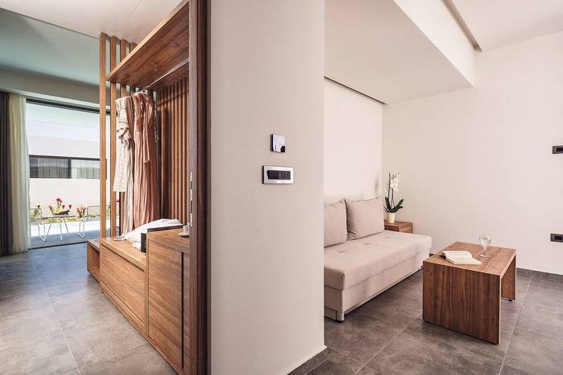 Innenansicht eines Zimmers im Lindos Grand Resort & Spa mit Couch, Tisch und Ankleidebereich.
