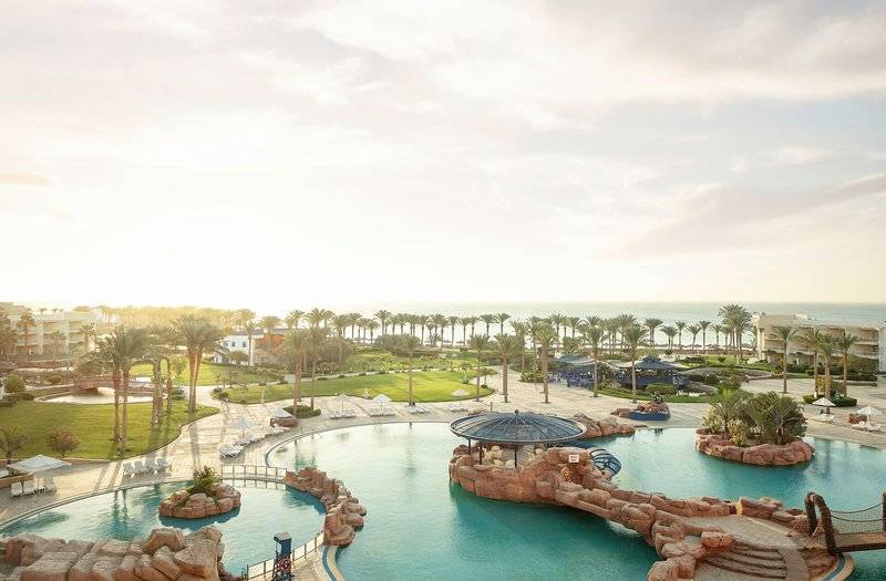 Außenansicht des Palm Royale Soma Bay Resorts mit Swimmingpools, Palmen und Meer im Hintergrund.