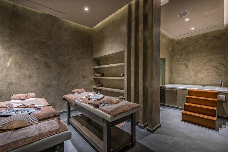 Massageraum im Alexandra Beach Resort mit zwei Massagetischen, einer Badewanne und Holztreppen.