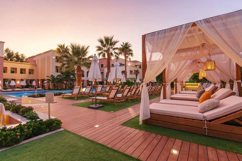 Samaina Inn Lounge-Terrasse bei Sonnenuntergang mit gepolsterten Liegen, weißen Vorhängen und einem Swimmingpool im Hintergrund.