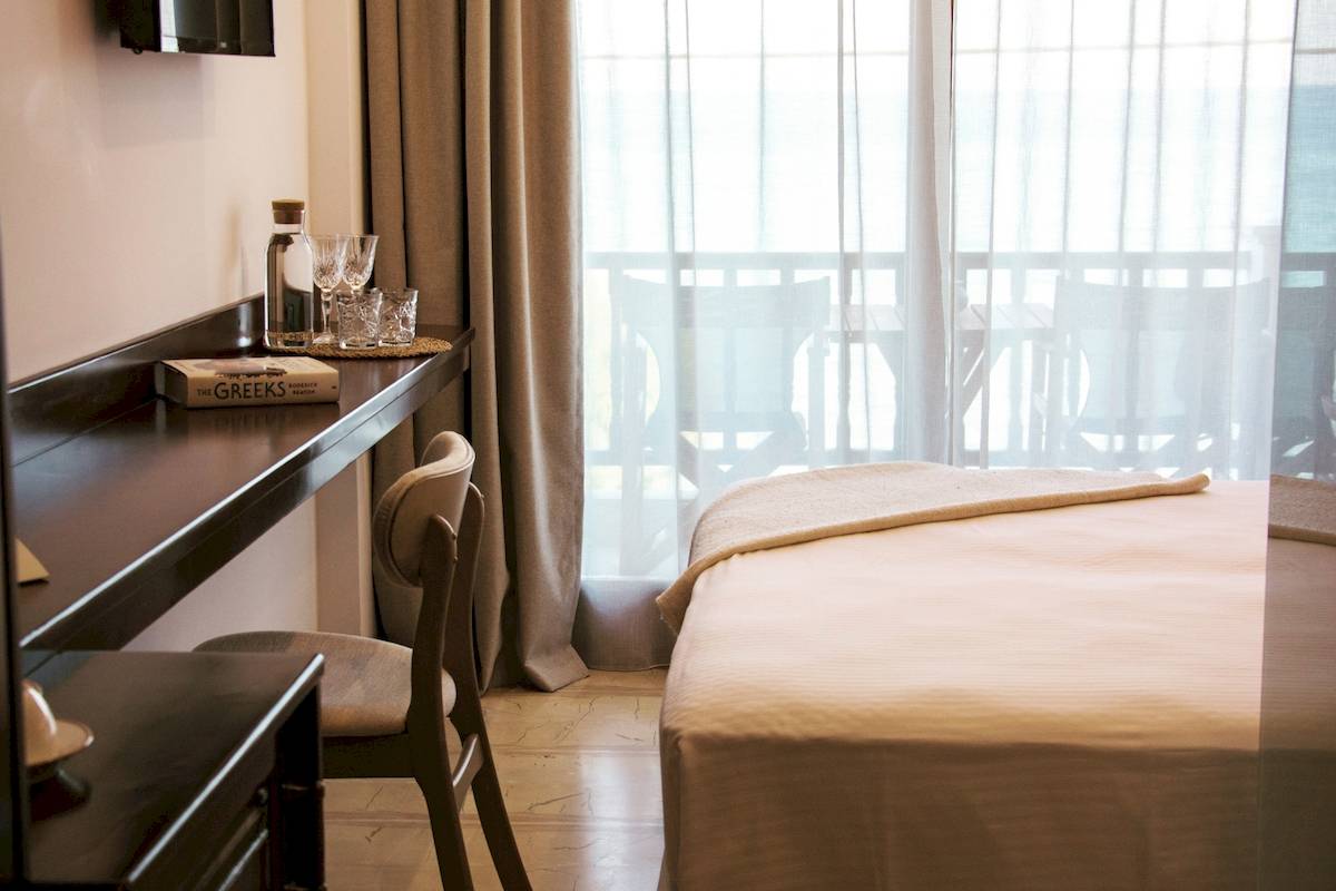 Ein Schlafzimmer im Sunrise Hotel Samos mit einem Bett, einem Schreibtisch und einem Fenster mit Blick auf eine Terrasse.