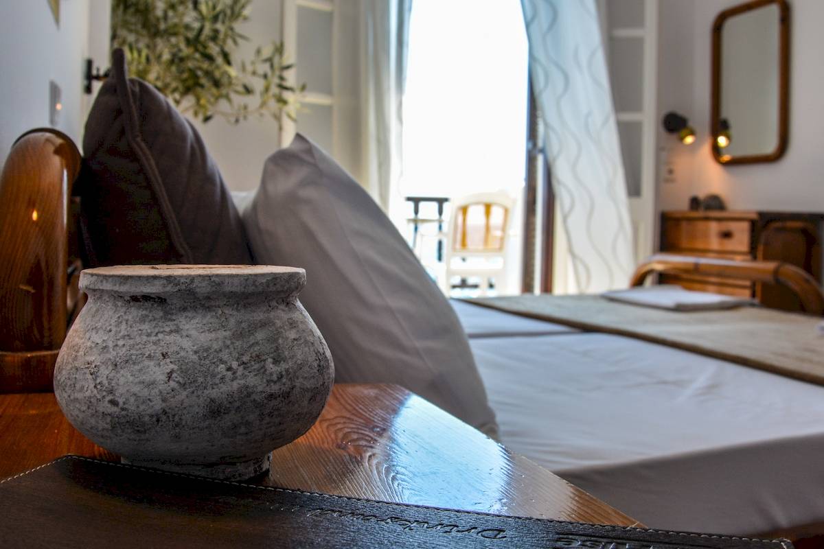 Doppelbett im Schlafzimmer des Sunrise Hotels Samos mit grauen Kissen und einer Vase auf dem Tisch.