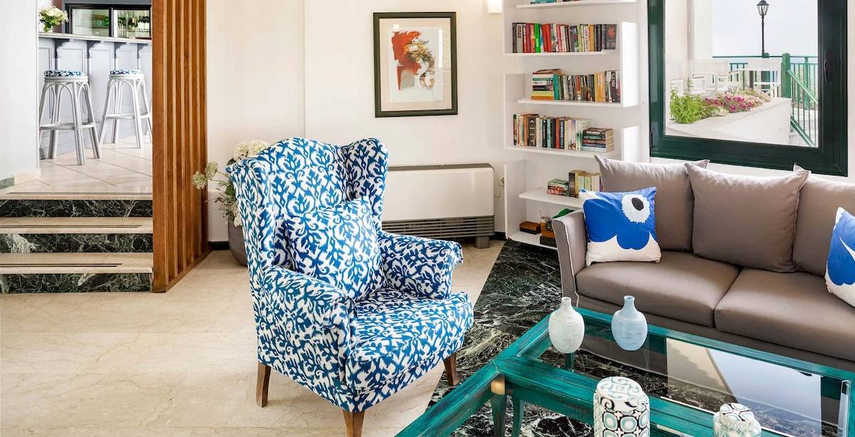 Wohnzimmer des Kalidon Panorama Hotels mit blauem Sessel, grauem Sofa und Bücherregal.