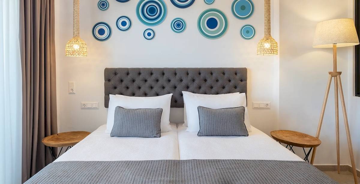 Doppelzimmer im Kalidon Panorama Hotel mit zwei Betten, Kissen, Decken, Nachttischen und dekorativen Kreisen an der Wand.