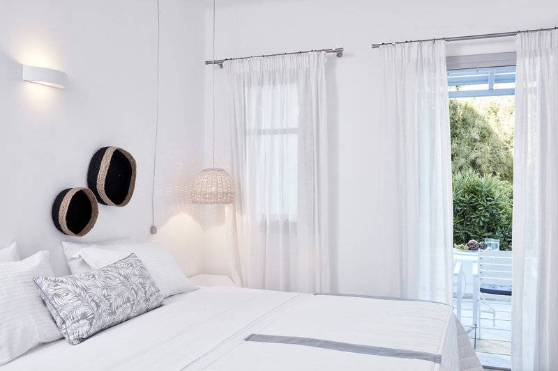 Schlafzimmer im Mr and Mrs White Paros Hotel mit weißen Möbeln und Vorhängen.
