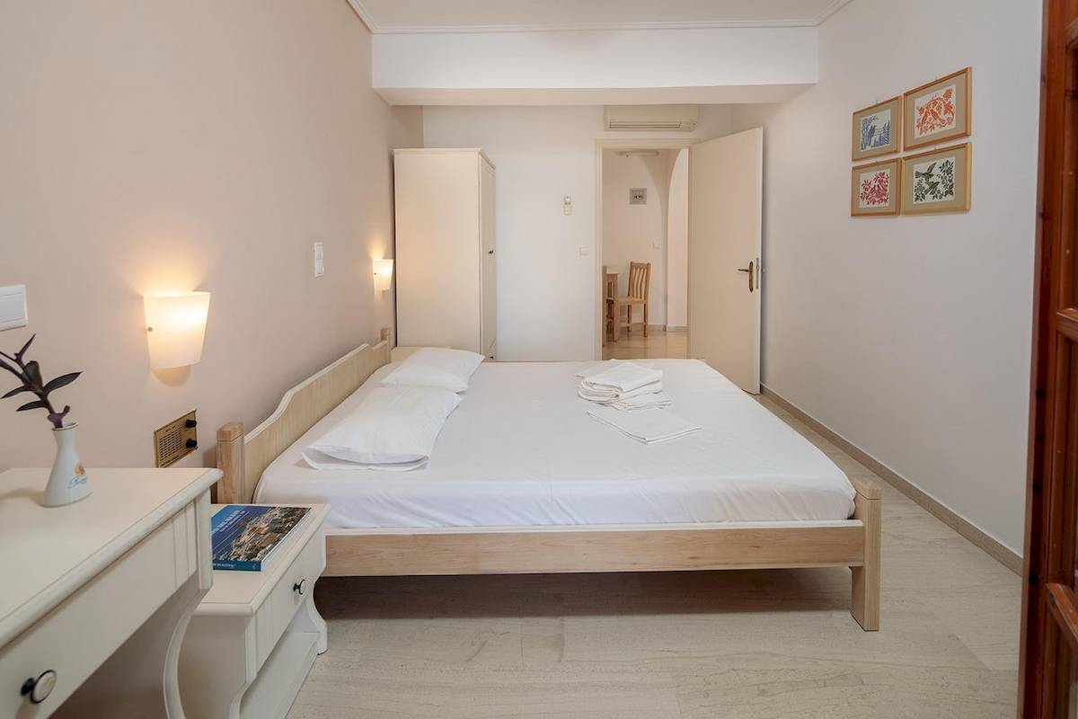 Schlafzimmer im Proteas Hotel mit einem Doppelbett, weißem Bettwäsche, Nachttisch mit Buch und Pflanze in einer Vase